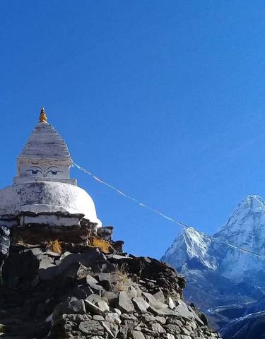 A stupa with prayer flags in a mountainous region covered with snow.