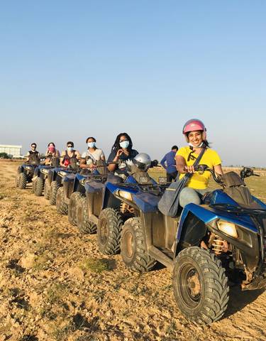 Group of people riding ATVs along a dirt path near a water body.