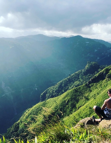 Person sitting on a mountainside with a scenic view.
