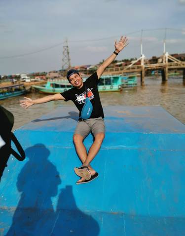 Person sitting on a blue boat with arms outstretched smiling.