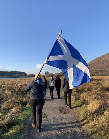 People with a large Scottish flag walking towards castle ruins.