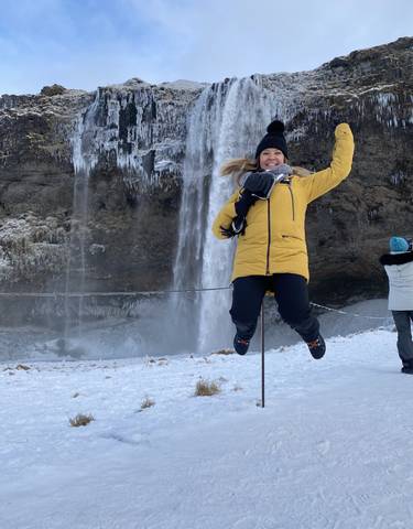Person jumping in front of a frozen waterfall.
