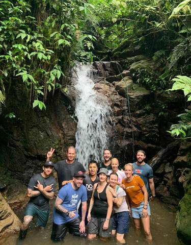 Group standing in front of a waterfall in a jungle setting.