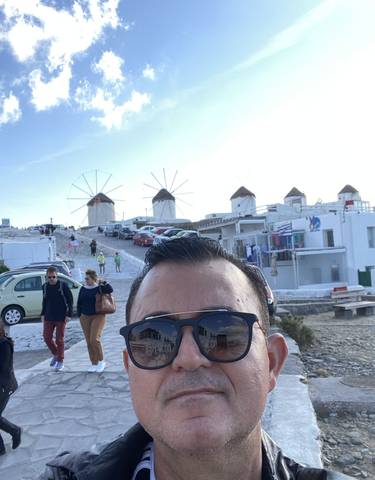 A man taking a selfie with the famous windmills in Mykonos in the background.