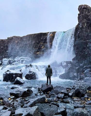 Person wearing a hood standing in front of a waterfall.
