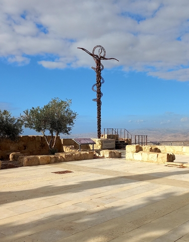 Ancient structure with a serpent sculpture and trees in an open area under a blue sky.