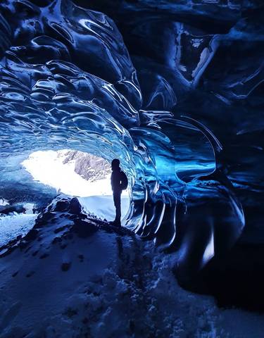 Person standing inside an ice cave with a view outside to a snowy landscape.