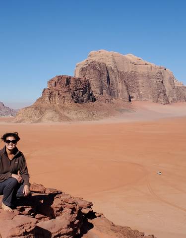 Person sitting on a rocky outcrop with a vast desert landscape in the background.