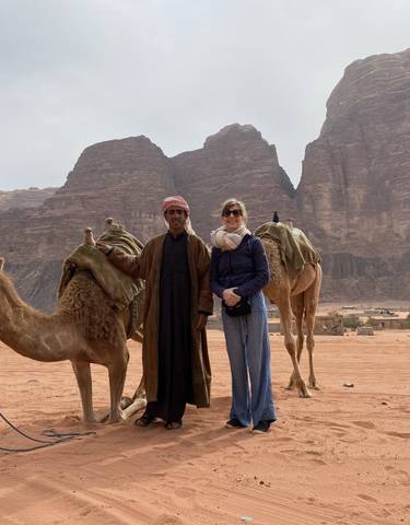 Two people with camels in the desert with rocky hills.