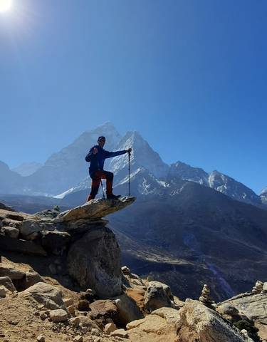 Hiker posing at the top of a peak with snowy mountains.