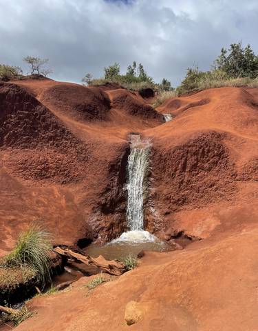 Small waterfall flowing through red soil formations.