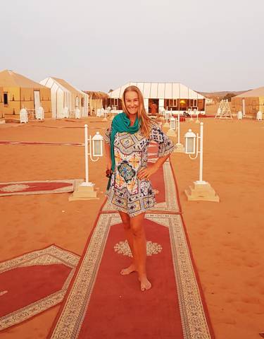 Smiling woman standing on a decorated path in a desert camp.