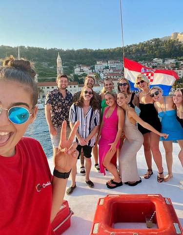A group of tourists posing on a boat with the Croatian flag, smiling.