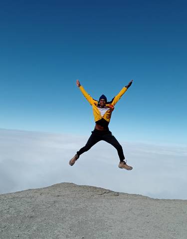 A person jumping with joy above the clouds on a mountain peak.