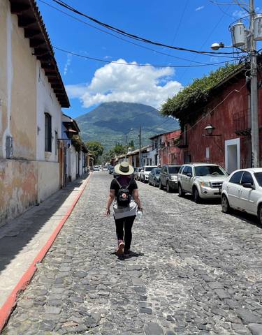 A person walking down a cobbled street with mountains in the background.