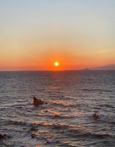 Sun setting over the ocean with a distant ship.