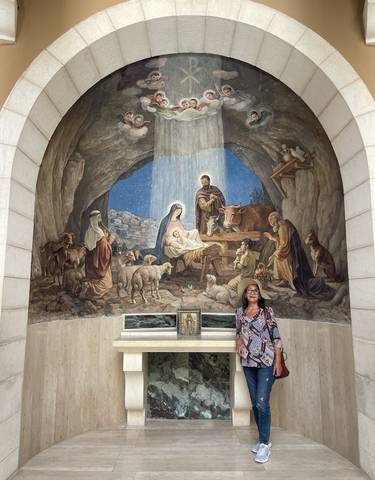 Woman standing in front of a large mural depicting the Nativity scene.