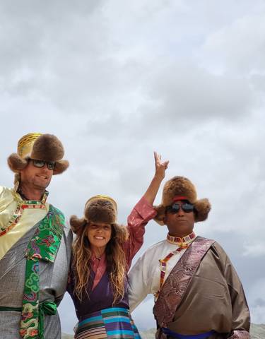 Three people wearing traditional attire with fur hats standing outdoors.