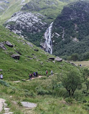 Hikers walking on a trail towards a waterfall.