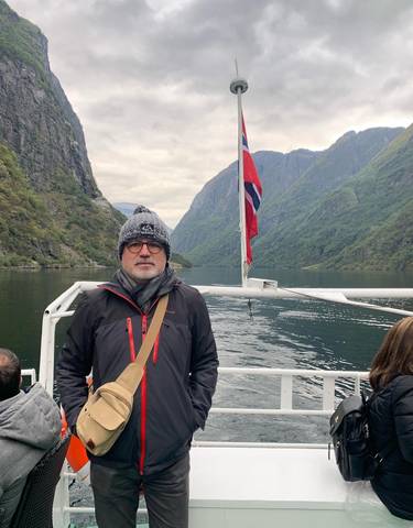 Person on a boat with a Norwegian flag and fjords in the background.