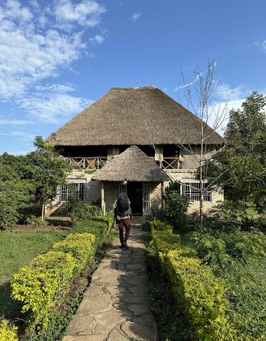 A person at the entrance of a traditional thatched-roof house.