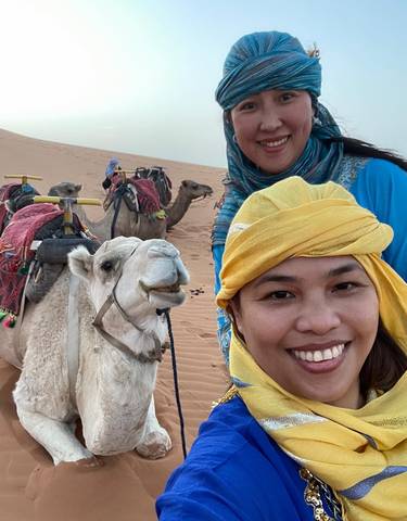 Smiling women with camels in the desert.