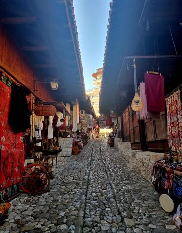 Cobblestone street lined with market stalls and colorful textiles.