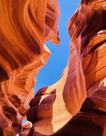 Canyon with smooth red curves and a bright blue sky visible above.