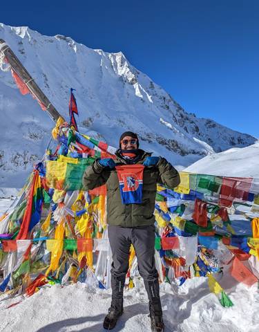 Person holding a flag in a snowy mountainous landscape with prayer flags.