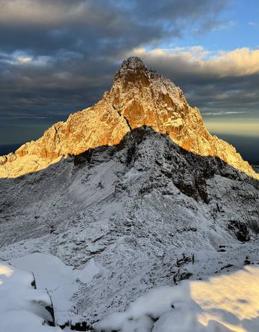 Snow-covered mountain at sunrise with dramatic shadows.