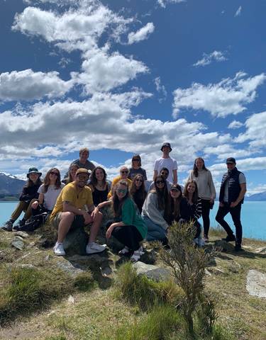 Friends gathered by a lakeside with mountains in the background.