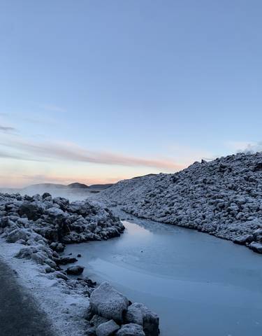 Snow-covered landscape with a still river, during sunset.