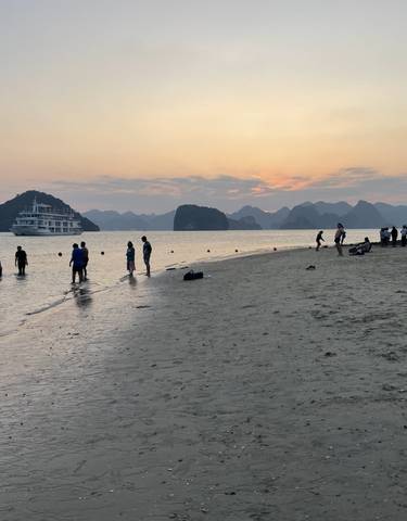 Beach scene at sunset with people and a cruise ship.