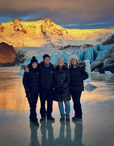 Group photo with people standing on icy ground against glacier background.