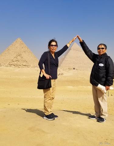 Two people posing with pyramids in the background, blue skies.