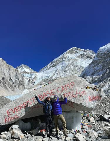 Tourists posing at the Everest Base Camp marker with high mountains.