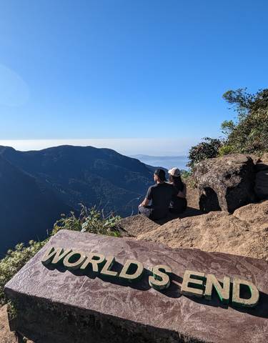 Two people sitting on a cliff with expansive views of mountains.