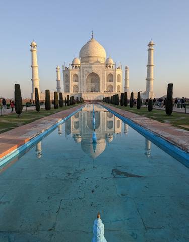 The Taj Mahal reflected in a long pool of water with a clear sky.