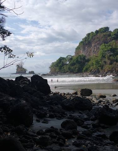 Coastal beach scene with rocky formations and people swimming.