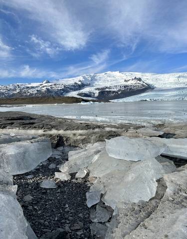 Frozen lake with ice chunks surrounded by snowy mountains.