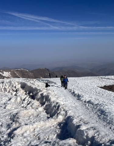 Hikers walking on a snow-covered mountain ridge with a view.