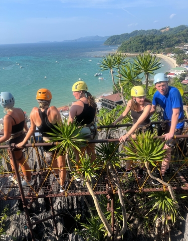 Group of people rock climbing with safety gear, overlooking a coastal town.