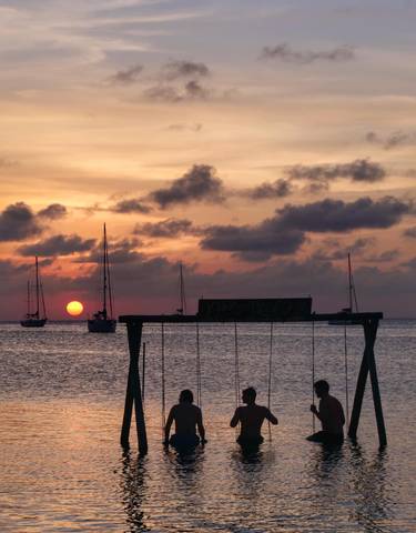 Sunset over the ocean with silhouettes of sailboats.