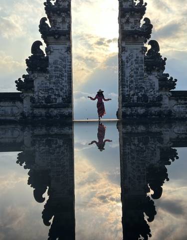 Silhouette of a person between two ancient structures, reflected in water.