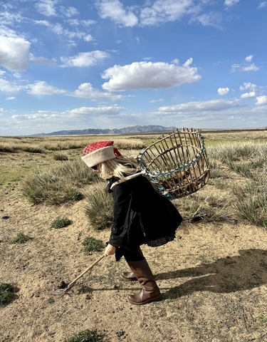 A woman carrying a large basket in a grassland.