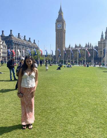 Person standing on a green field with flags and historic buildings.