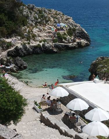 People enjoying a rocky beach with clear water in a cove.