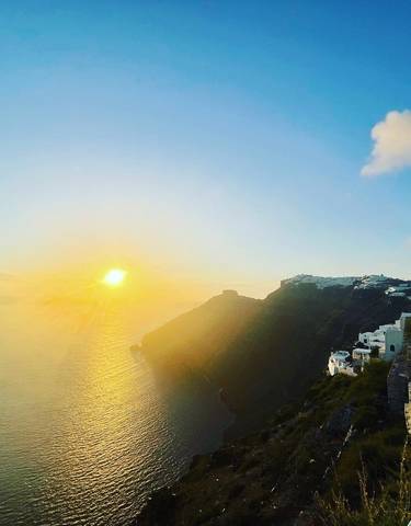 Dramatic sunset over the Aegean Sea with architectural structures on a cliff.