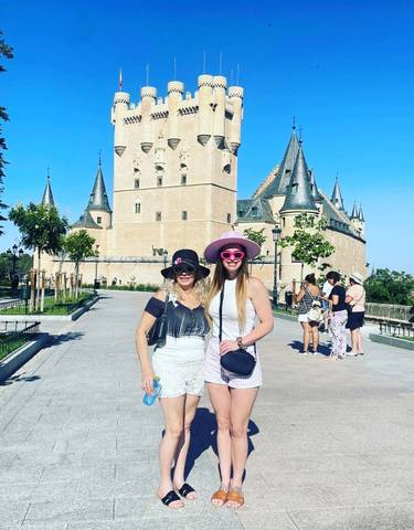 Two people posing in front of a historic castle with spires and turrets.