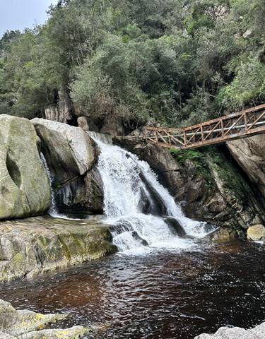 A waterfall with rocks and a metal bridge above.